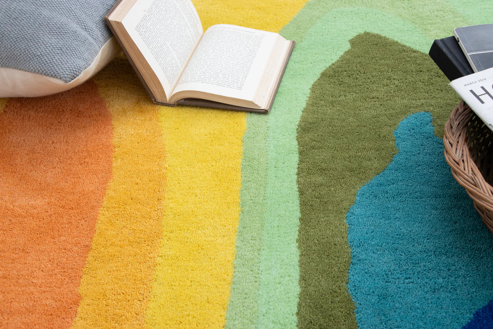 Colorful gradient rug with a book and pillow on a wooden floor.