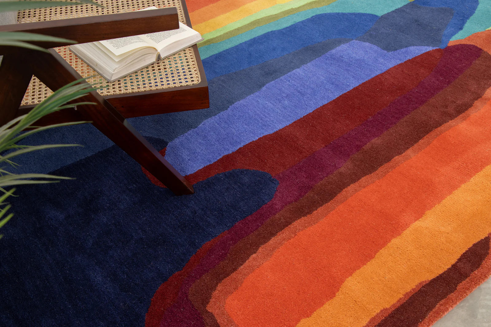 Colorful abstract rug with gradient colors next to a wicker chair and book.